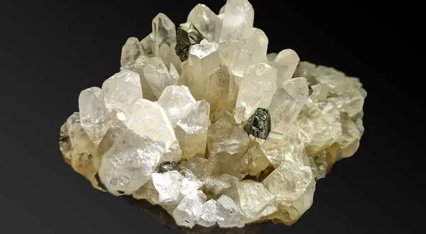 Ein Cluster aus klaren Quarzkristallen mit eingelagerten dunklen Mineralien. Die Quarz-Bedeutung liegt in seiner Klarheit und Reinheit, die oft mit Energie und Heilung assoziiert wird.