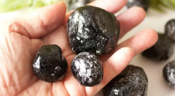 Eine Hand hält mehrere glänzende, schwarze Apachentränen-Steine. Sie sehen aus wie kleine, dunkle Tropfen.