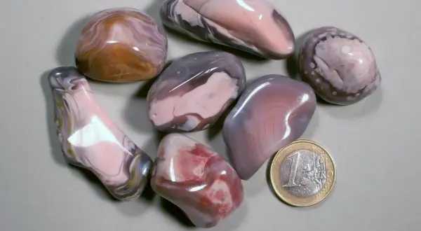 Glatt geschliffene Botswana Achat Steine in Rosa-, Grau- und Brauntönen, daneben eine 1-Euro-Münze.