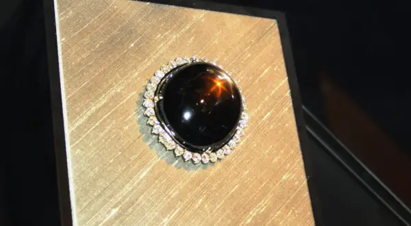 Ein glänzender schwarzer Saphir mit einem Stern-Effekt, umgeben von kleinen Diamanten. Seine geheimnisvolle schwarzer saphir bedeutung fasziniert.