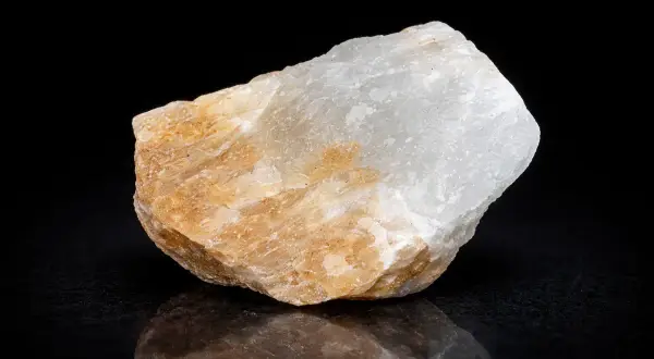 Ein Stück Alabaster, dessen Bedeutung in seiner Reinheit und seinem sanften Glanz liegt, schimmert in Weiß und Beige vor schwarzem Hintergrund.