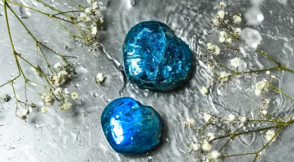 Zwei herzförmige Apatit Edelsteine glänzen unter Wassertropfen, umgeben von zarten weißen Blüten.