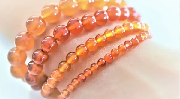 Armbänder aus leuchtenden, orange-roten Feuerachat-Kugeln in verschiedenen Größen, die wie ein warmer Sonnenuntergang auf der Haut liegen.