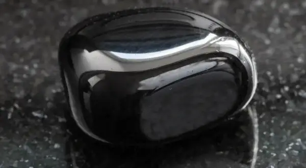 Glatter, glänzender onyx stein liegt auf einer dunklen, gesprenkelten Oberfläche.
