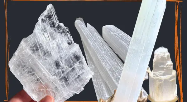 Mehrere transparente, säulenförmige Kristalle, die wie Eis aussehen. Ein großer, flacher Selenit Stein wird von einer Hand gehalten.