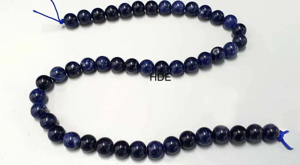 Eine Kette aus tiefblauen Sodalith-Perlen, die auf einem weißen Hintergrund liegen.