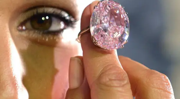 Ein riesiger, pinker Diamantring wird von einer Hand gehalten. Man fragt sich, wie viel kostet ein Kilo Diamant?