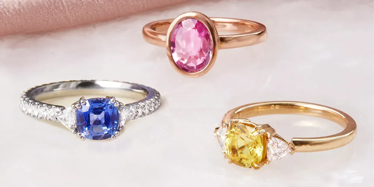Drei Ringe mit Edelsteinen: ein blauer Saphir, ein gelber Saphir und ein rosa Saphir. Die Bedeutung von rosa Saphir steht für Liebe und Mitgefühl.