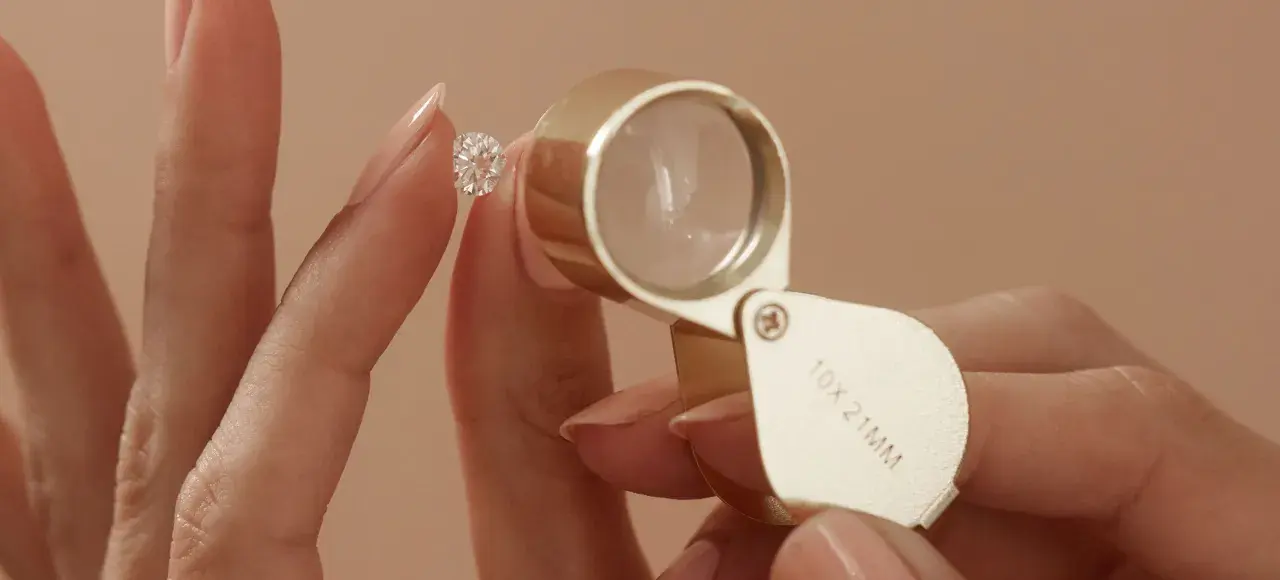 Eine Hand hält einen funkelnden Diamanten, während eine Lupe ihn vergrößert. Ein perfekter einschluss diamant wird genau geprüft.
