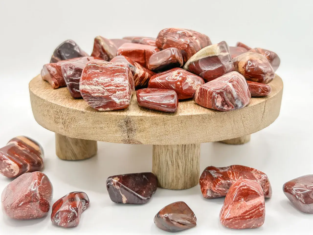Rote und braune Jaspissteine, die die Bedeutung von Kraft und Vitalität symbolisieren, liegen auf einem Holzpodest und drumherum.