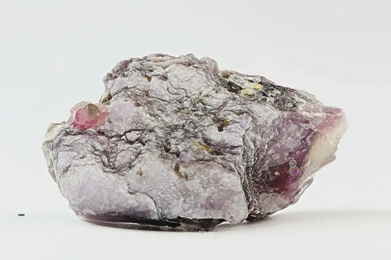Ein schuppiger, lila-grauer Lepidolith-Stein mit glänzenden Oberflächen und einem kleinen, rosa Kristall.