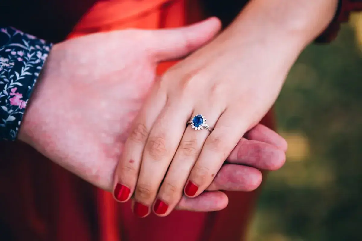 Ein Ring mit einem tiefblauen Saphir und kleinen Diamanten, gehalten von zwei Händen.