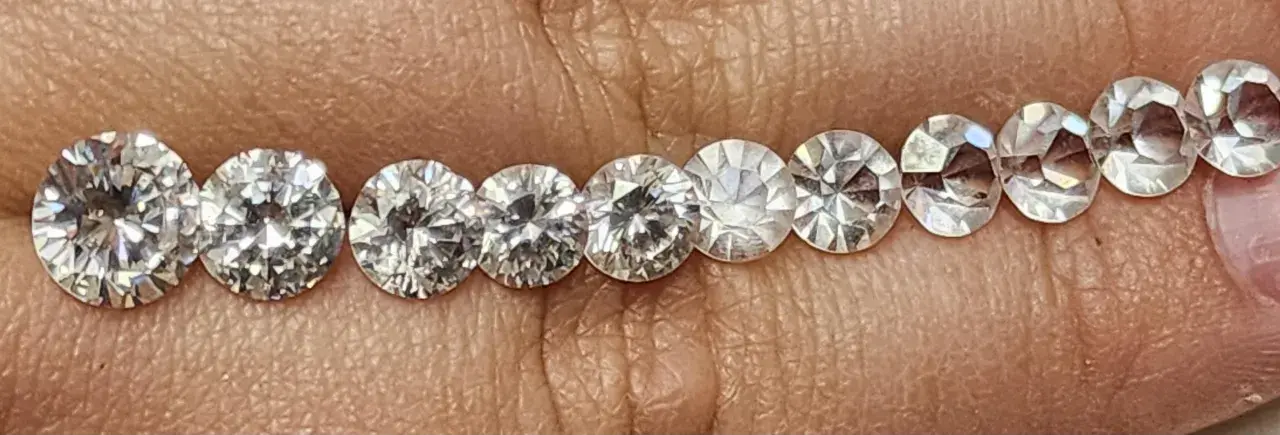 Reihe von geschliffenen Steinen, die auf einer Hautoberfläche liegen. Es ist schwierig, diamant oder zirkonia erkennen, da sie sehr ähnlich aussehen.