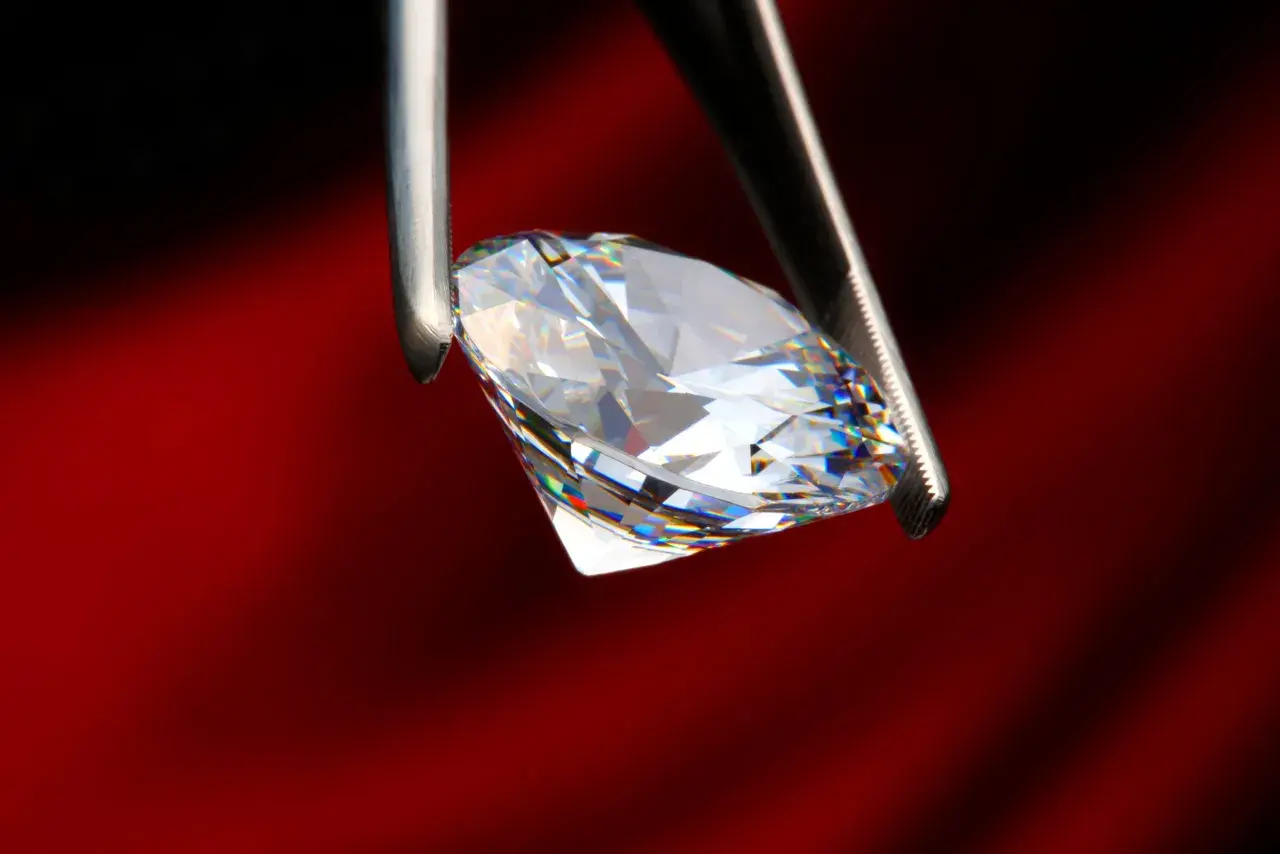 Ein funkelnder Diamant, gehalten von einer Pinzette, zeigt sein gesamtes Spektrum an Farben. Was ist ein brillant? Ein Stein, der Licht bricht und verzaubert.