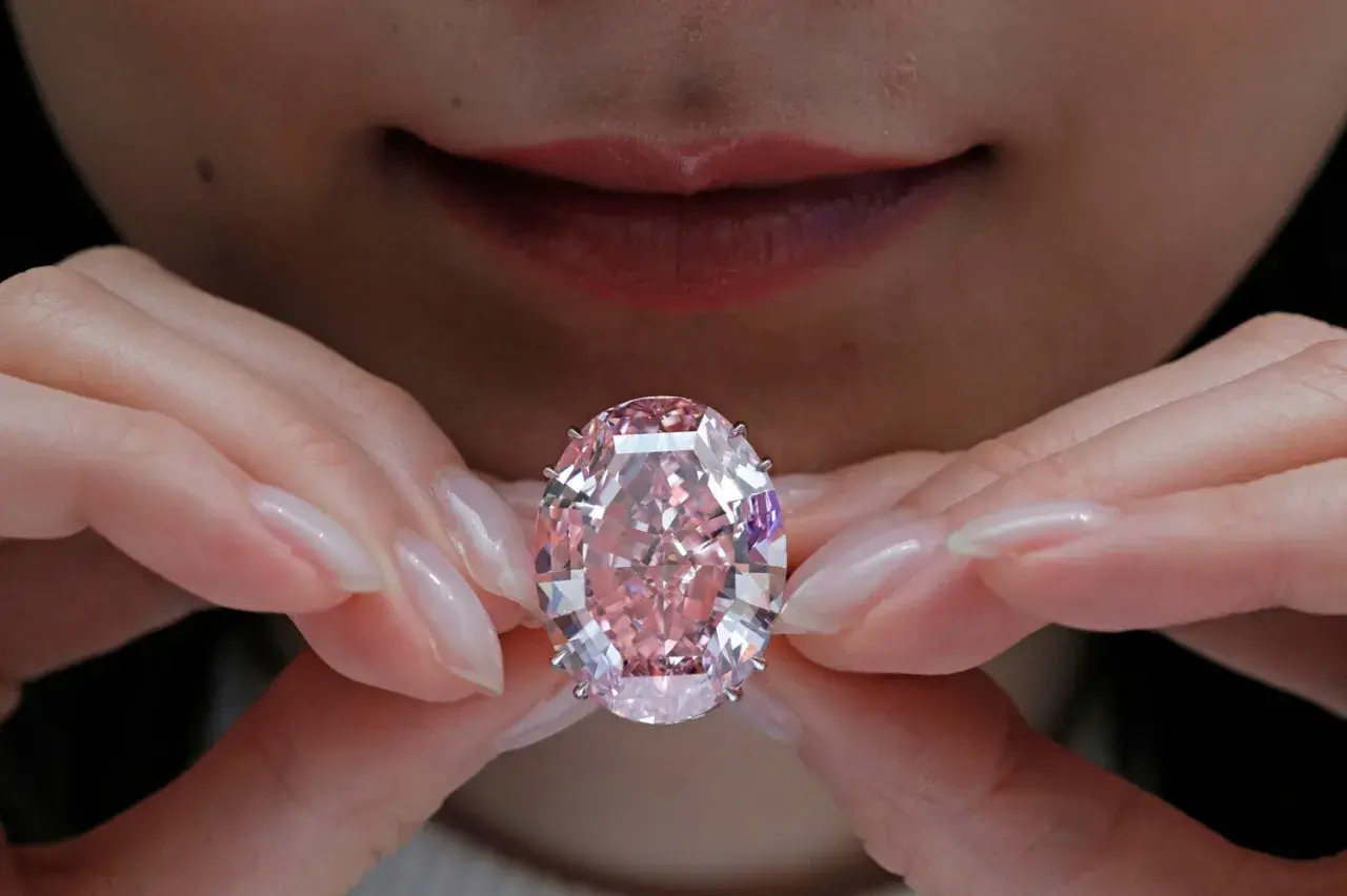 Hände halten einen rosafarbenen Diamanten. Welche Diamanten Farbe ist die teuerste? Rosa Diamanten sind extrem selten und wertvoll.