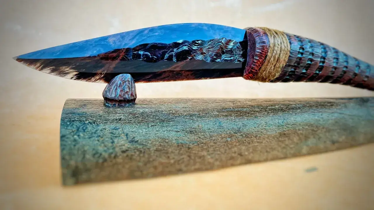 Ein Messer mit einer Klinge aus glänzendem, blau-braunem Obsidian, das an einem geschnitzten Holzgriff befestigt ist.