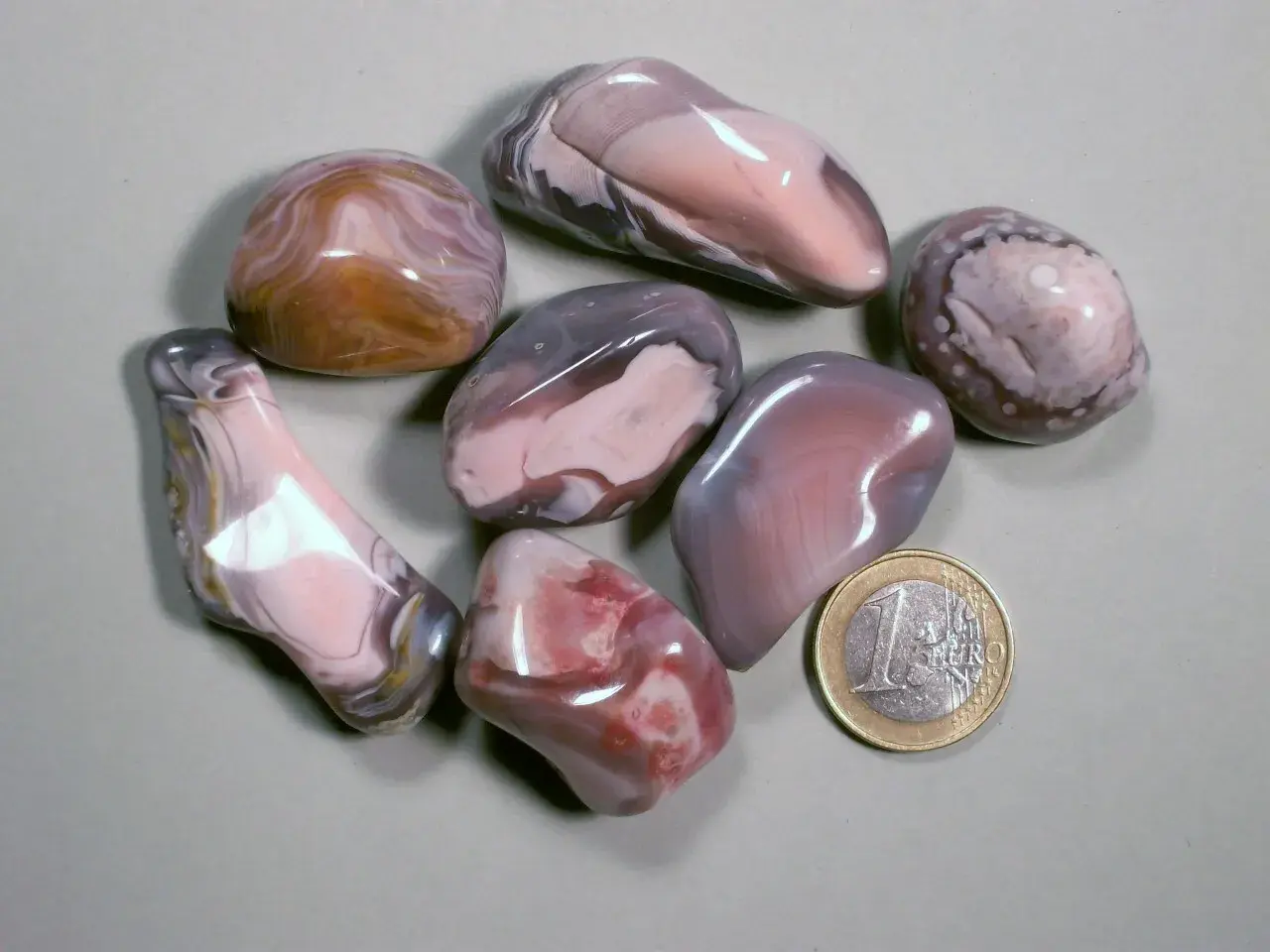 Glatt geschliffene Botswana Achat Steine in Rosa-, Grau- und Brauntönen, daneben eine 1-Euro-Münze.