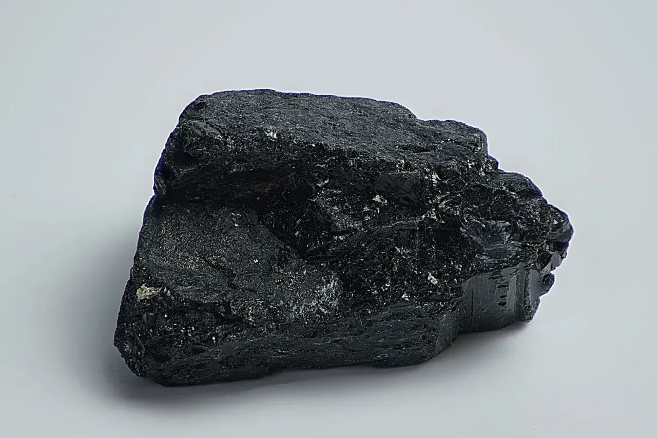 Ein glänzender, schwarzer Stein, der an einen Brocken Onyx erinnert, liegt auf weißem Grund.