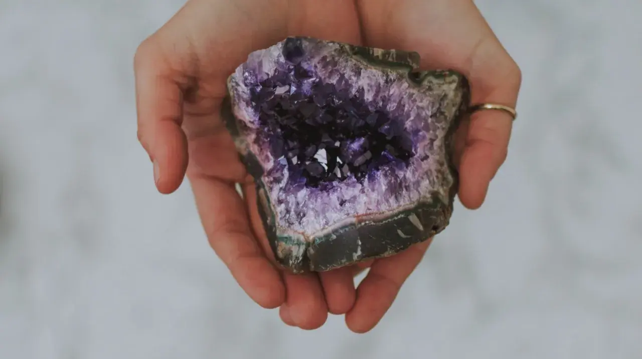 Hände halten einen tiefvioletten Amethyst. Seine Wirkung auf die Haut wird oft als beruhigend beschrieben.