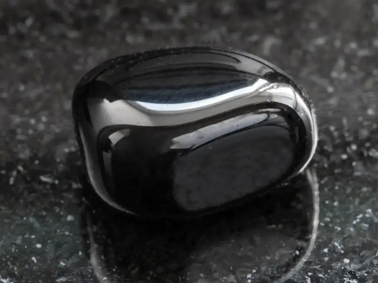 Glatter, glänzender onyx stein liegt auf einer dunklen, gesprenkelten Oberfläche.