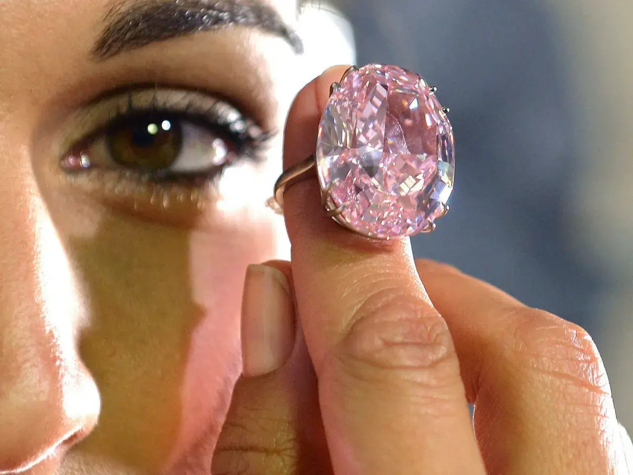Ein riesiger, pinker Diamantring wird von einer Hand gehalten. Man fragt sich, wie viel kostet ein Kilo Diamant?