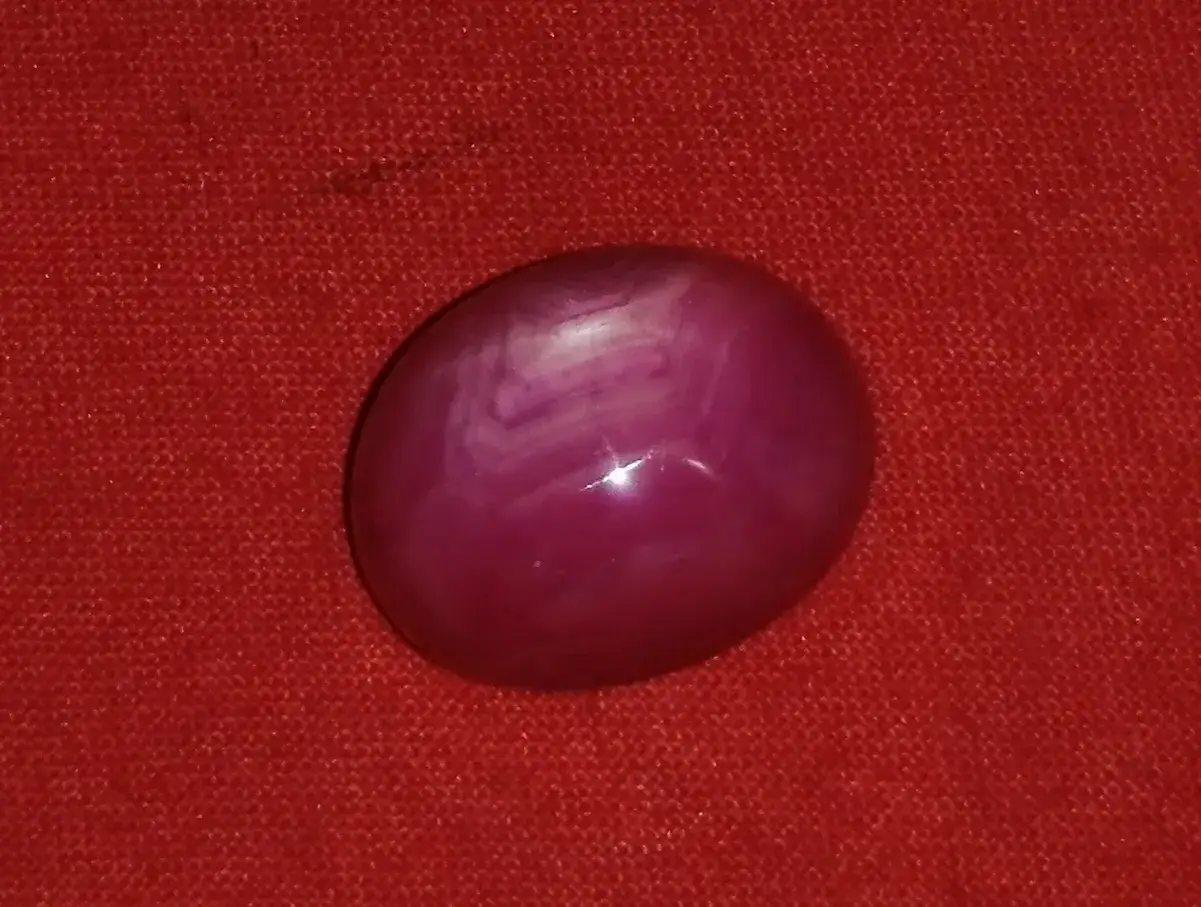 Ein glatter, ovaler sternrubin mit einem faszinierenden Muster auf rotem Stoff.