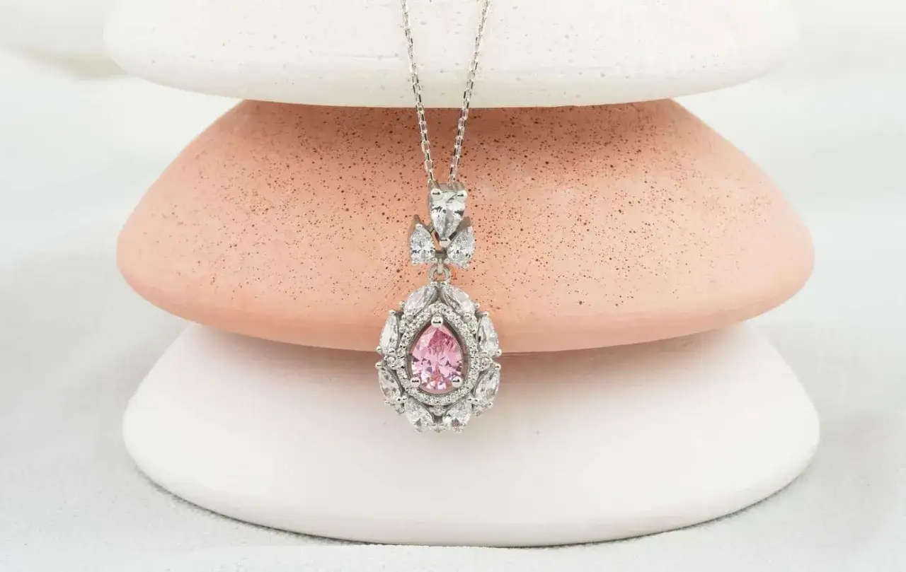 Ein zartes Collier mit einem tropfenf&ouml;rmigen rosa Saphir, umgeben von funkelnden Zirkonia. Die Bedeutung von rosa Saphir steht f&uuml;r Liebe und Mitgef&uuml;hl.