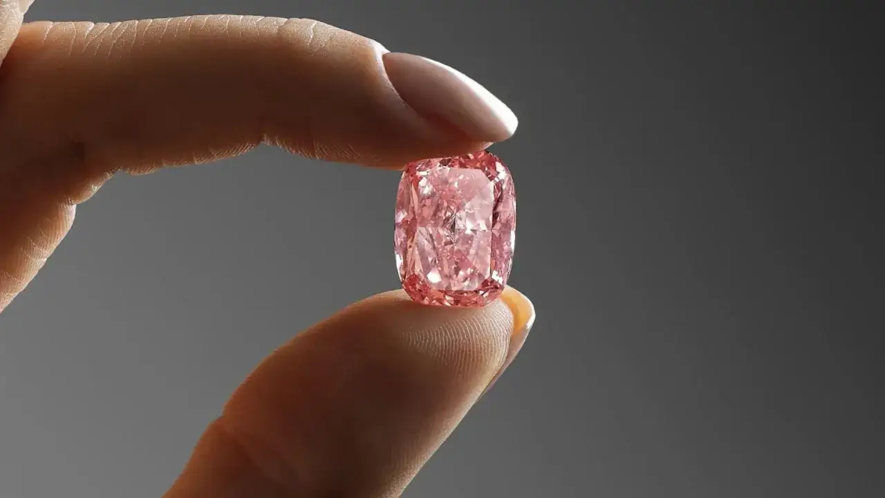 Ein Finger h&auml;lt einen leuchtend pinken Diamanten, der wie der teuerste Diamant der Welt aussieht. Sein Preis ist unvorstellbar.