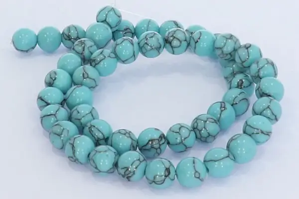 Eine Kette aus hellblauen, runden Perlen mit dunklen Äderungen, die an den Himmel erinnern. Der türkis schimmert in der Sonne.