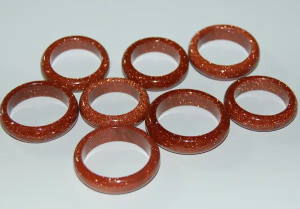A collection of eight shimmering goldfluss stein rings, each a warm, coppery brown with flecks of gold.