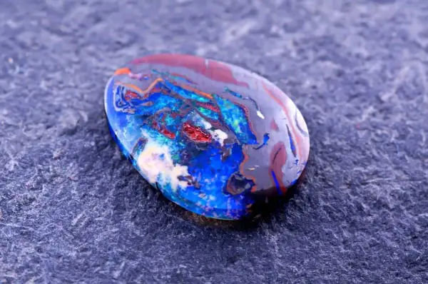 Ein faszinierender Edelstein aus Australien, ein Boulderopal, zeigt ein lebendiges Farbspiel aus Blau, Rot und Orange auf dunklem Grund.