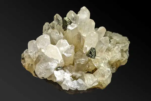 Ein Cluster aus klaren Quarzkristallen mit eingelagerten dunklen Mineralien. Die Quarz-Bedeutung liegt in seiner Klarheit und Reinheit, die oft mit Energie und Heilung assoziiert wird.
