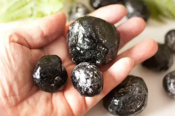 Eine Hand hält mehrere glänzende, schwarze Apachentränen-Steine. Sie sehen aus wie kleine, dunkle Tropfen.