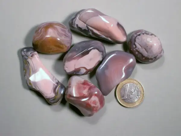 Glatt geschliffene Botswana Achat Steine in Rosa-, Grau- und Brauntönen, daneben eine 1-Euro-Münze.