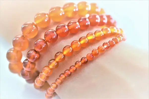 Armbänder aus leuchtenden, orange-roten Feuerachat-Kugeln in verschiedenen Größen, die wie ein warmer Sonnenuntergang auf der Haut liegen.