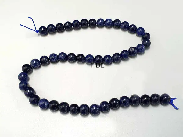 Eine Kette aus tiefblauen Sodalith-Perlen, die auf einem weißen Hintergrund liegen.