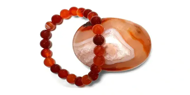 Armband aus Karneol-Kugeln, die die positive karneol wirkung symbolisieren. Daneben ein polierter Karneol-Stein.
